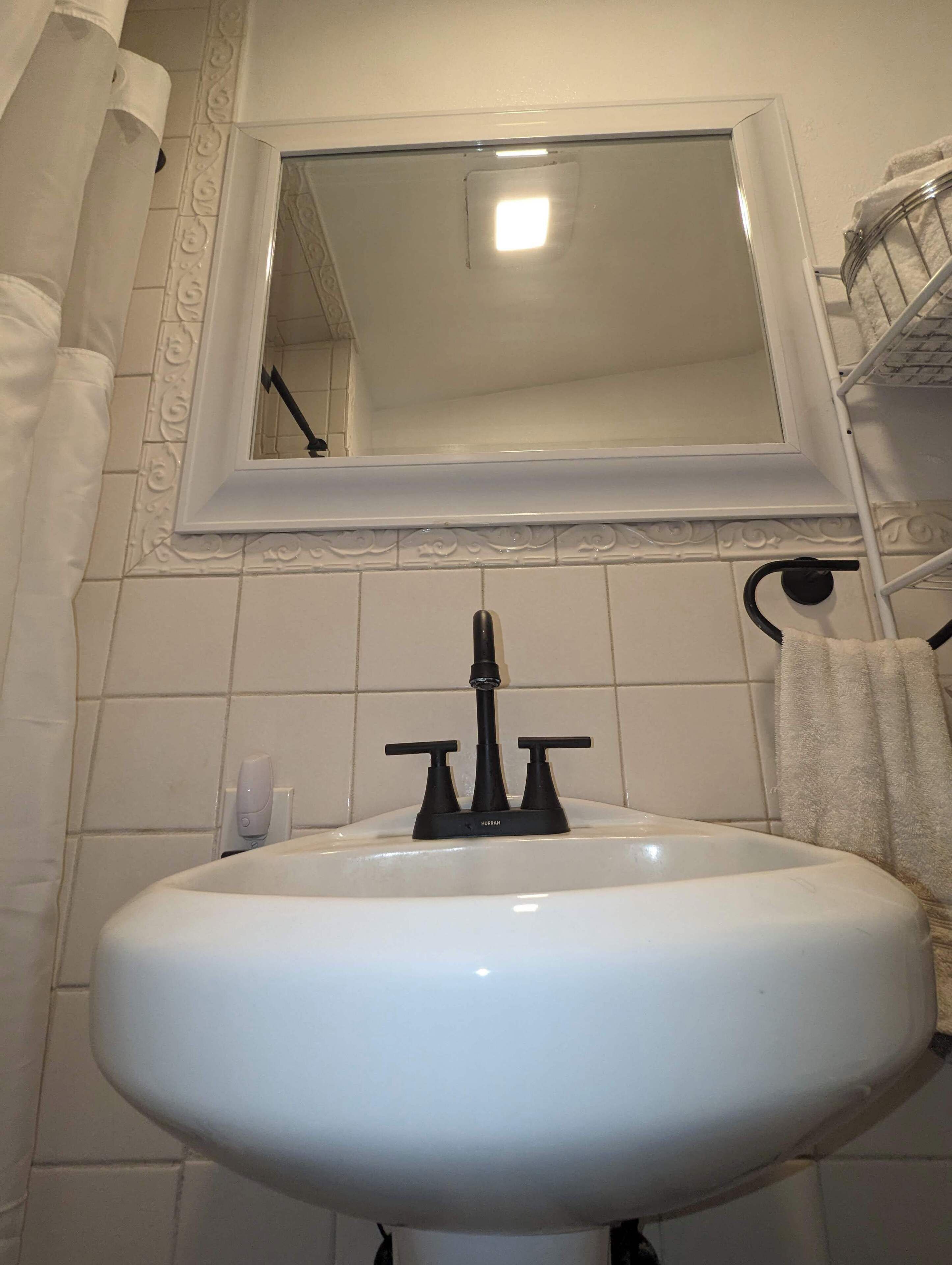 Une salle de bain avec un lavabo blanc, un miroir au-dessus et un porte-serviettes sur la droite.