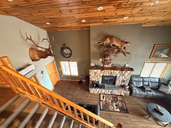 A living room with a stone fireplace, a wooden staircase, and mounted animal heads on the walls. - Spacious 3-bedroom building in Cow creek SD close to Outpost Lodge with AC (Pierre)