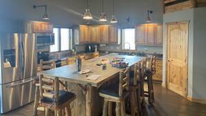A spacious kitchen with wooden cabinets, stainless steel appliances, and a large island with bar stools. - Spacious 3-bedroom building in Cow creek SD close to Outpost Lodge with AC (Pierre)