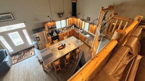 A spacious kitchen with wooden cabinets, a central island, and a dining area with wooden chairs. - Spacious 3-bedroom building in Cow creek SD close to Outpost Lodge with AC (Pierre)
