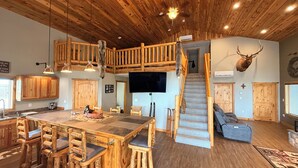 A rustic interior with a wooden staircase, a large dining table, and a mounted deer head. - Spacious 3-bedroom building in Cow creek SD close to Outpost Lodge with AC (Pierre)