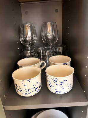 Una estantería con varios vasos de vino y tazas de cerámica.