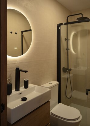 Un baño moderno con un lavamanos blanco, grifo negro y ducha con mampara de vidrio.