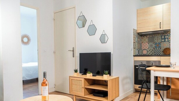Ett modernt vardagsrum med en TV, ett träskåp och ett runt bord med en flaska på.