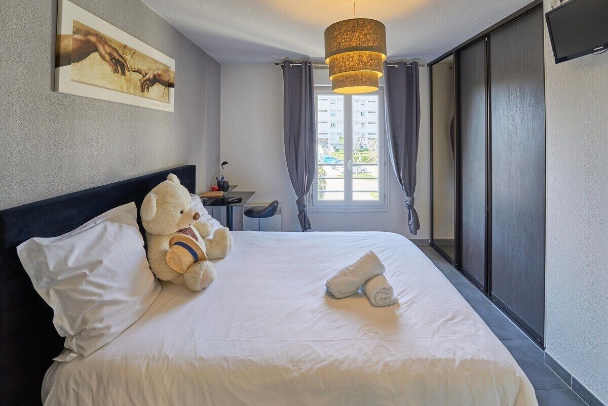 Een hotelkamer met een bed, een teddybeer, een schilderij, een bureau en een schuifdeur.
