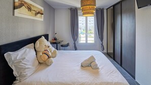 Une chambre d’hôtel avec un lit, un ours en peluche, un tableau, un bureau et une porte coulissante.