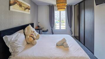 Een hotelkamer met een bed, een teddybeer, een schilderij, een bureau en een schuifdeur.