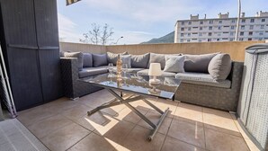 Une terrasse extérieure avec une table à plateau en verre, des sièges rembourrés de couleur grise et une lampe.