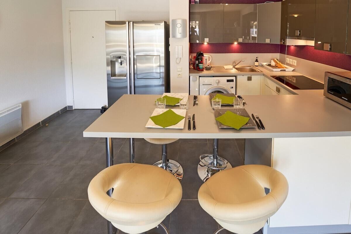 Een moderne keuken met roestvrijstalen apparatuur, een eettafel met stoelen en een zichtbare wasmachine.