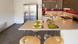 Une cuisine moderne équipée d’appareils électroménagers en acier inoxydable, une table à manger avec des chaises et un lave-linge visible.