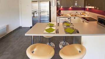 Een moderne keuken met roestvrijstalen apparatuur, een eettafel met stoelen en een zichtbare wasmachine.