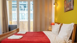 Quarto de hotel com cama, mesa de cabeceira, luminária e janela com cortinas.