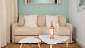 A beige sofa with two pillows, a small white table with two wine glasses and a bottle, and a mirror on the wall. - Le Corsaire : Relaxing Stay, Beach & Pool (Carqueiranne)