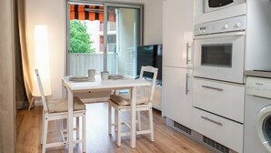 A compact kitchen with a dining table, chairs, a microwave, oven, and a washing machine. - Le Corsaire : Relaxing Stay, Beach & Pool (Carqueiranne)