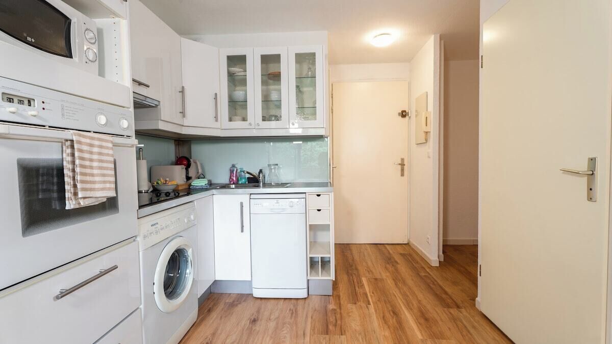 A compact kitchen with a washing machine, oven, microwave, and cabinets.