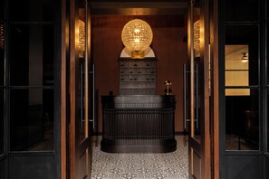 A hallway with a reception desk, a decorative chandelier, and a patterned floor. - Merchant's Gate Songwat (Bangkok)