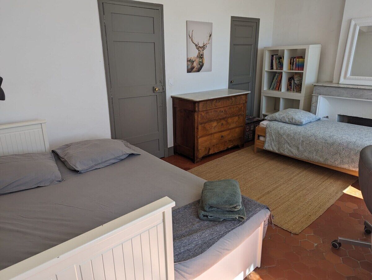 A bedroom with two beds, a dresser, a bookshelf, and a deer artwork on the wall.