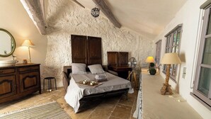 A bedroom with a stone wall, wooden bed, bedside tables, and a window. - Charming mansion (Toulon)