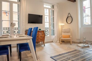 A dining area with a table set for two, a television mounted on the wall, and a window with shutters. - Rue des Arts - Stylish getaway & animals ok (Toulon)