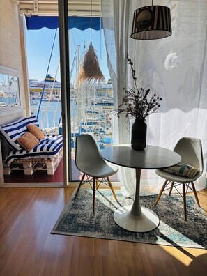 Habitación con vista a un puerto deportivo, un sofá a rayas, una mesa redonda con sillas y una lámpara colgante.