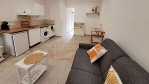 Une cuisine moderne équipée d’un lave-linge, un coin repas avec une table et des chaises, et un canapé gris agrémenté d’un coussin à motifs.