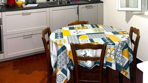 A kitchen with a microwave, toaster, kettle, sink, and a table with a patterned tablecloth.