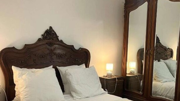 A neatly made bed with white linens, a wooden headboard, and a large mirror.