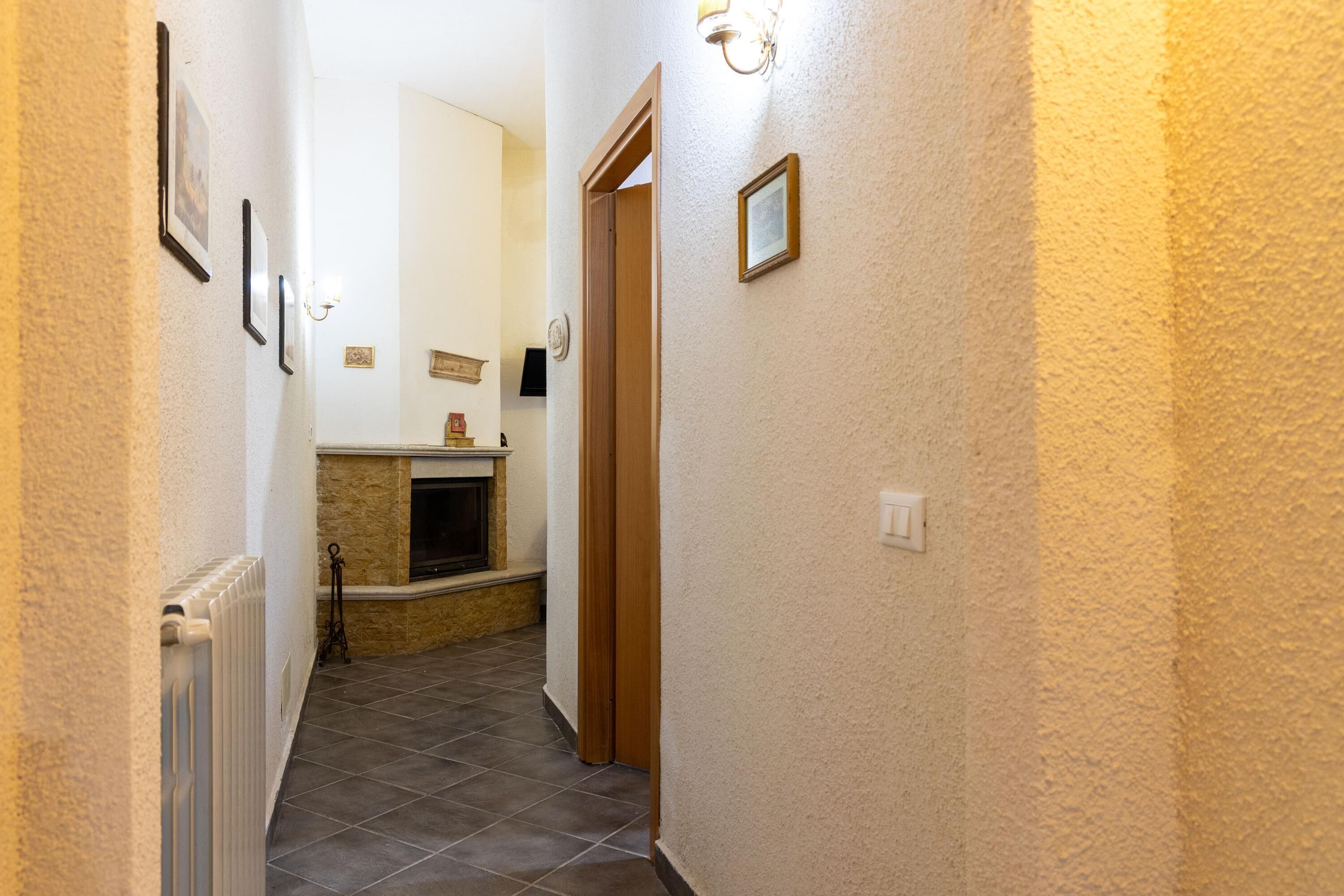 A narrow hallway with a radiator, a fireplace, and a door leading to another room.