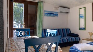Una habitación con una cama, una mesa, sillas, un sofá, un cuadro y un aire acondicionado.