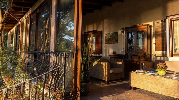 Una habitación iluminada por el sol, con un ventanal grande, un banco de madera, una mesita de mimbre y una planta en maceta.
