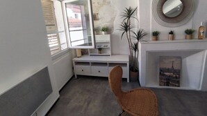 A room with a white console table, a wicker chair, a fireplace with a framed picture, and a round mirror on the wall. - Studio Horizon Toulon - near port & arsenal (Toulon)