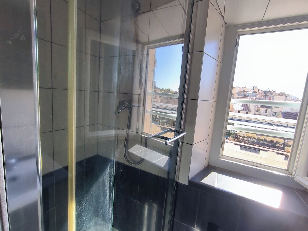 A glass-enclosed shower with a view of buildings outside.