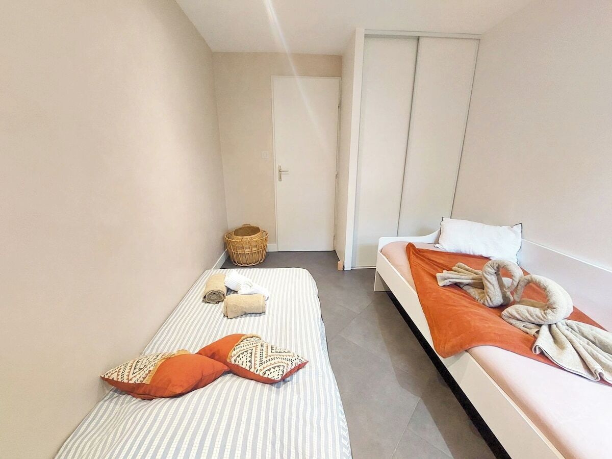 Une petite chambre propre, avec deux lits, une armoire et un panier.