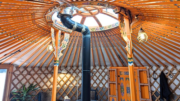 A traditional yurt with a circular wooden frame, a central black pole, and a patterned ceiling. - Ace Mongolian Yurt (Saint Anns)