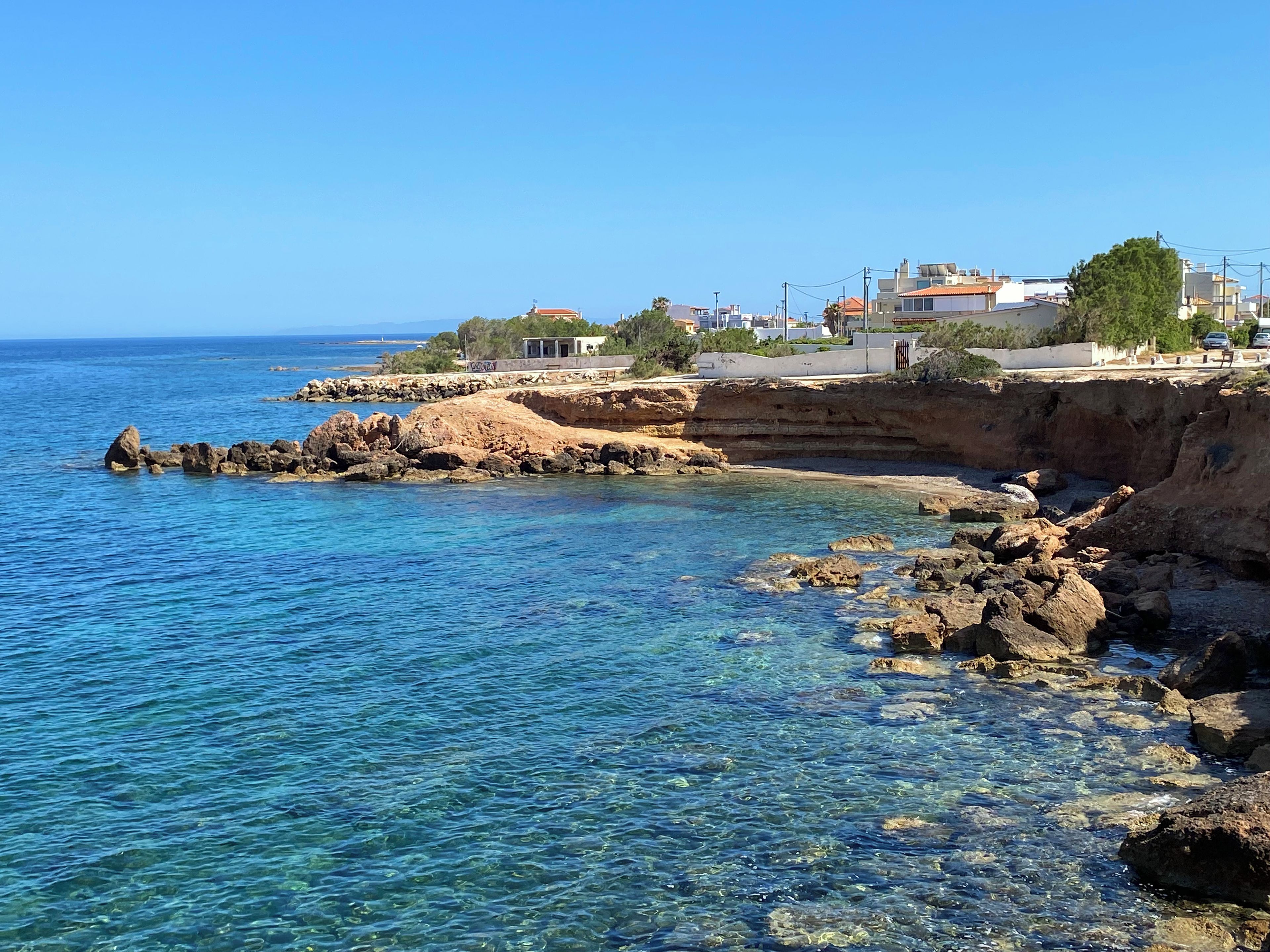 A coastal area with clear blue waters, rocky shoreline, and residential buildings.