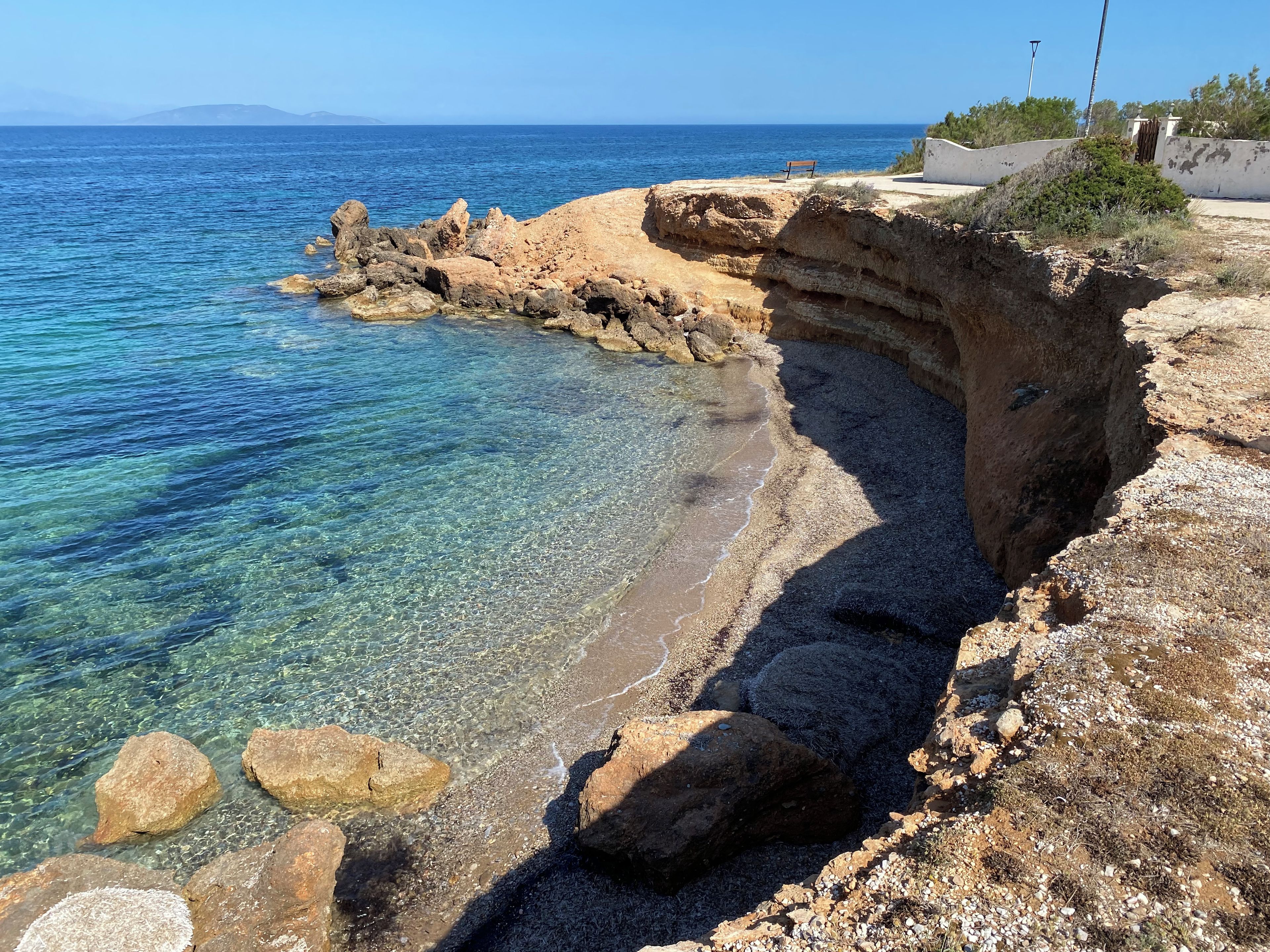 Paisatge marítim amb aigües blaves cristal·lines, terreny rocos i una boscana amb vista al mar.