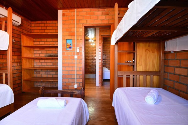 A room with two beds, wooden furniture, brick walls, and a small hallway leading to another room.