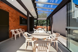 Eine überdachte Terrasse mit Tisch und Stühlen, einer Glastür und einer Ziegelwand.