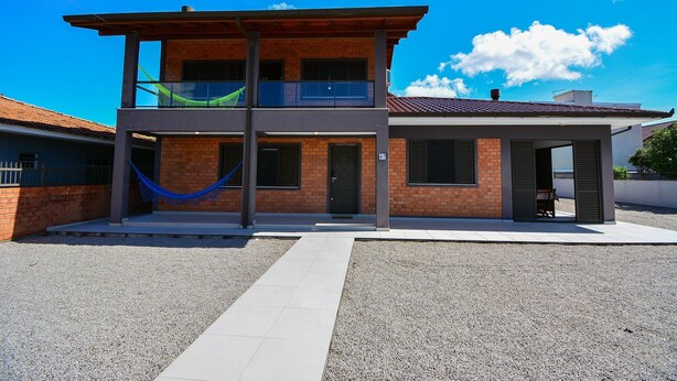 A two-story house with a balcony, a front door, and a small porch area. - Casa no Campeche a 300m do Mar - SDI019 (Florianópolis)