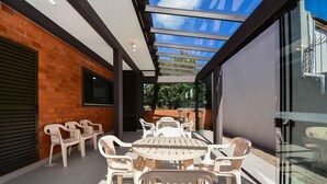 A covered patio with a table and chairs, a glass door, and a brick wall. - Casa no Campeche a 300m do Mar - SDI019 (Florianópolis)