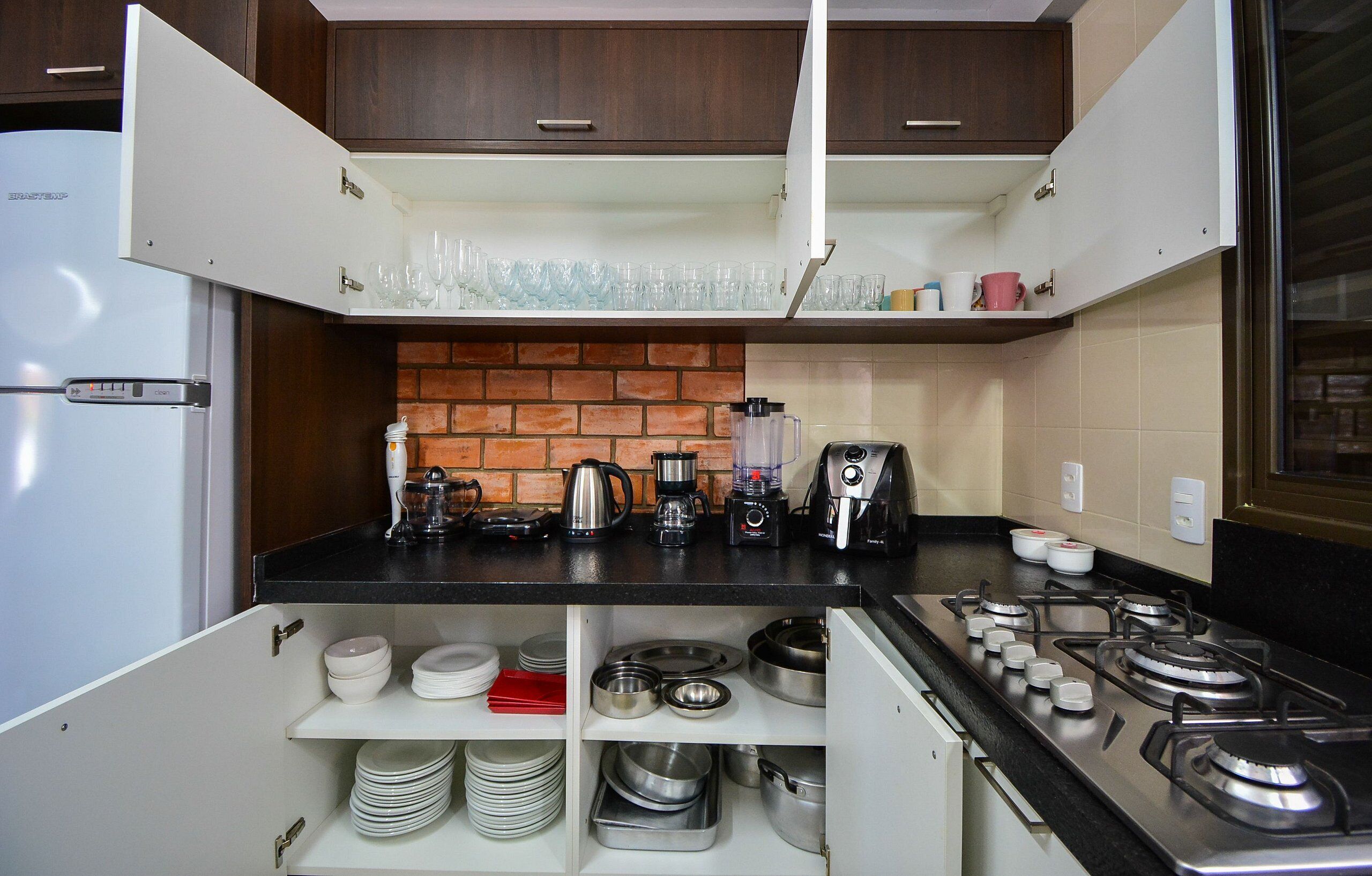 A compact kitchen with a refrigerator, coffee maker, blender, and gas stove.