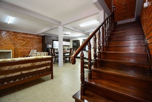 Uma escadaria com guarda-corpos de madeira, uma parede de tijolos e um sofá numa sala com chão em azulejos.