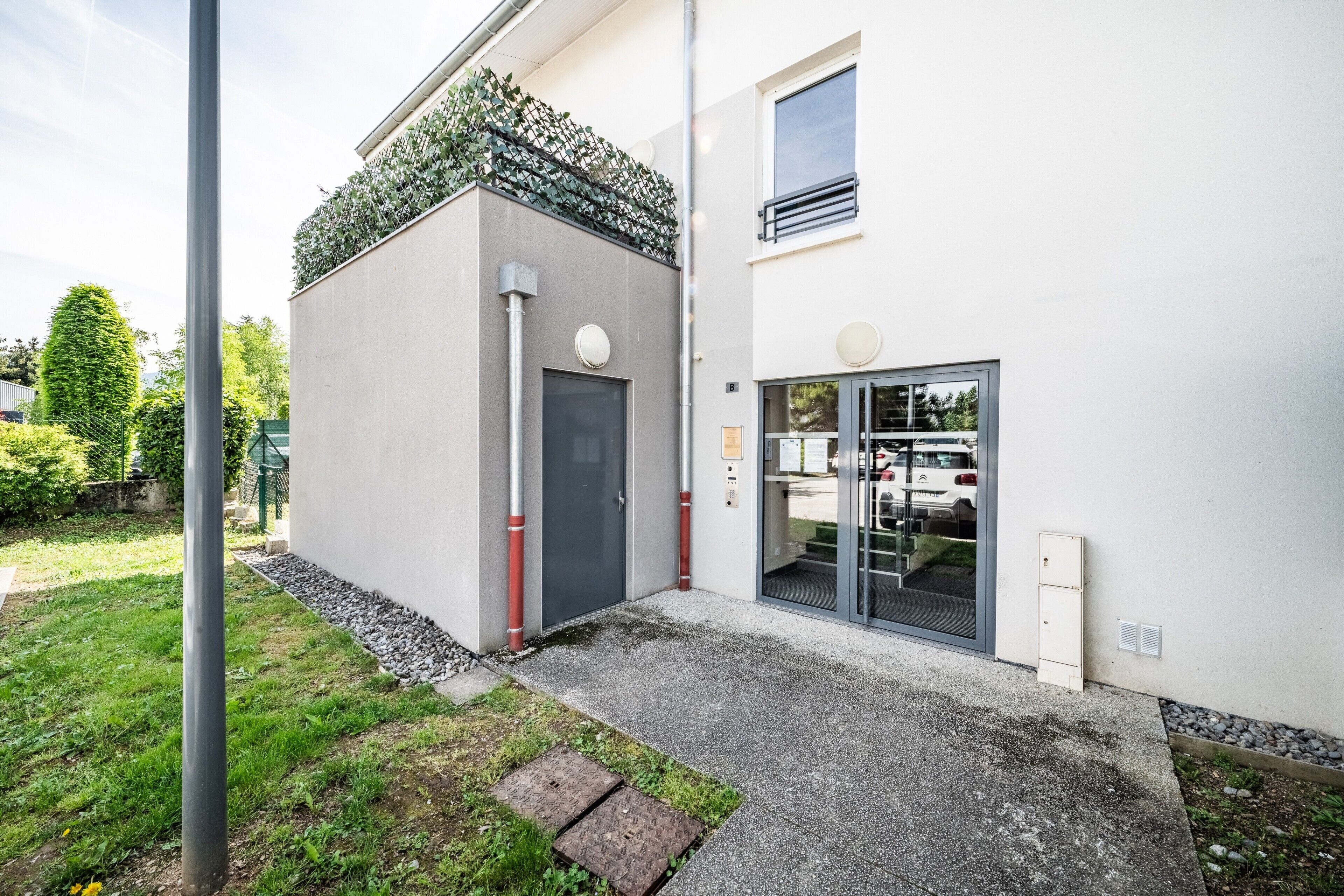 Un bâtiment moderne avec une porte grise, une petite fenêtre et un espace d’entrée pavé.
