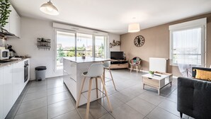 A modern kitchen with a central island, a dining area with a sofa, and a TV. - Apartment "Le Cocon" with Mountain View, Balcony, and Wi-Fi (Thonon-les-Bains)