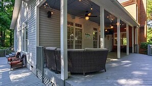 Eine überdachte Veranda mit Sitzgelegenheiten im Freien, einem Deckenventilator und einem Backsteinhaus im Hintergrund.