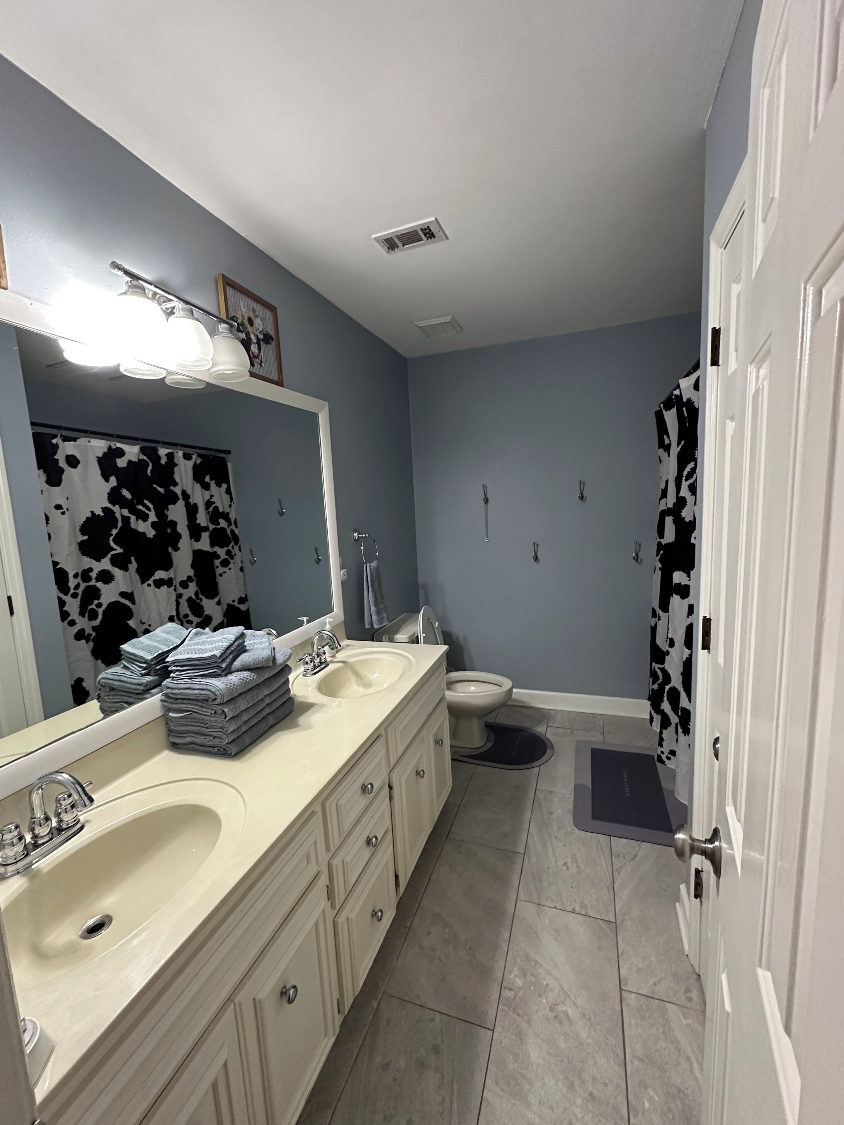 A bathroom with a double sink, a toilet, a mirror, and a shower curtain.