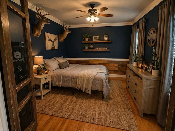 A bedroom with a bed, wooden headboard, a nightstand, a dresser, a ceiling fan, and wall-mounted deer antlers.