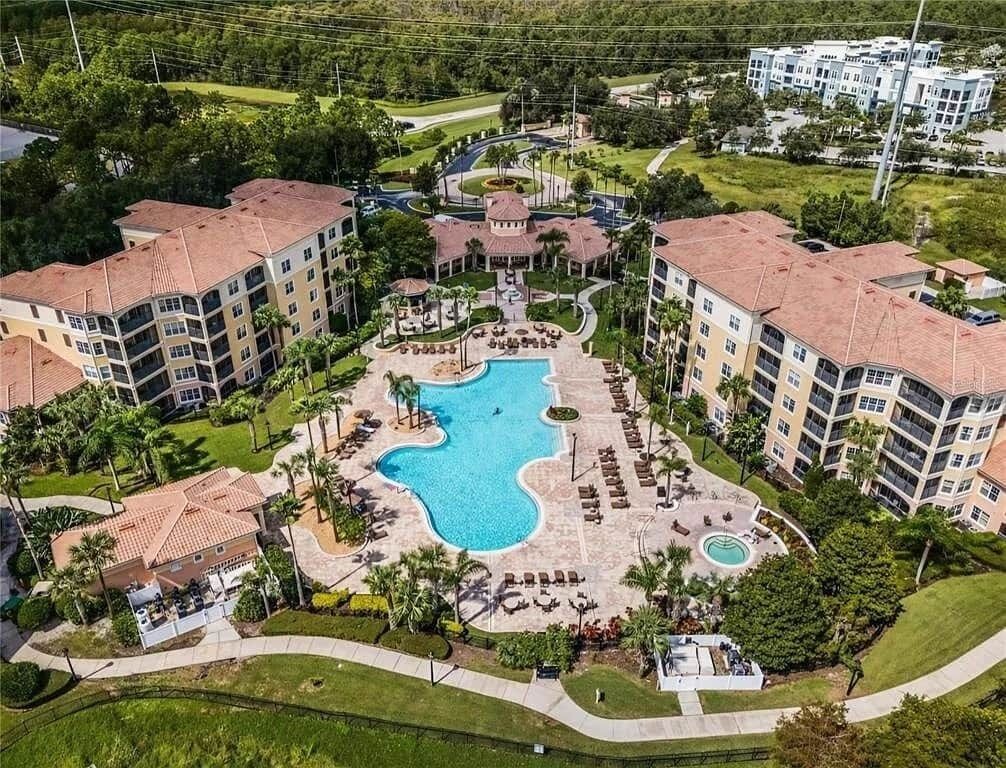 Um hotel com piscina central, várias varandas e vegetação ao redor.