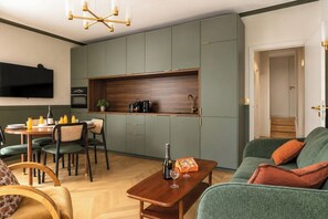 Ein kompakter Wohnbereich mit Essbereich, einer Couch, einem an der Wand montierten Fernseher und einer Küchenzeile mit Schränken und Arbeitsplatte.