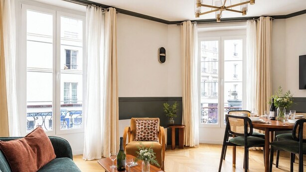 A living room with a sofa, a coffee table with a book and glasses, a fireplace, and a dining area with chairs and a table. - TheBlueStay 272 - Stunning Apartment in Paris 6 (Paris)
